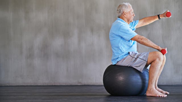 Ein älterer Mann sitzt auf einem Gymnastikball und trainiert mit Kurzhanteln.