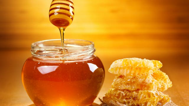 Ein mit Honig gefüllten Glas, darüber ein Honiglöffel, von dem Honig ins Glas tropft. Daneben Bienenwaben aus Wachs. Das Symbolbild vermittelt erfolgreich und nachdrücklich die Botschaft: Honig!