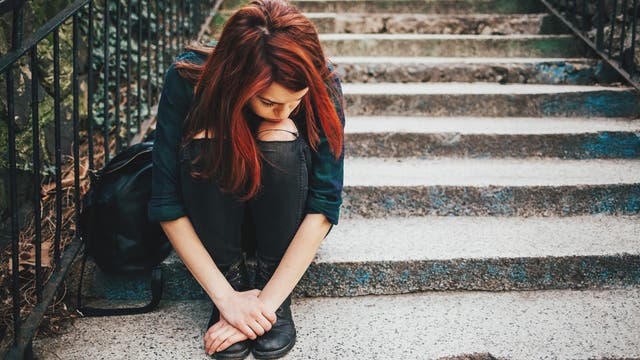 Eine traurige Jugendliche sitzt allein mit gesenktem Kopf auf einer Treppe