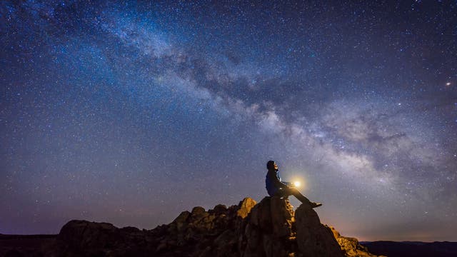 Ein Mann sitzt auf einem Fels und schaut auf die Milchstraße