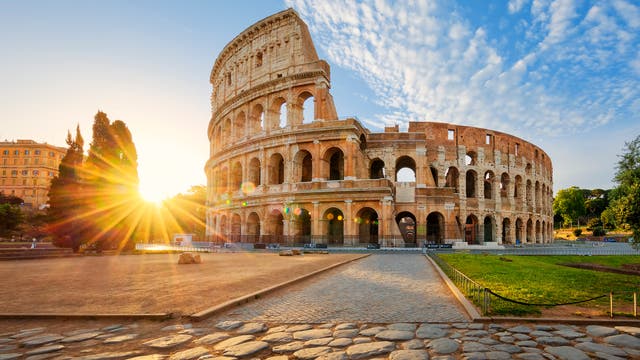 Hinter dem Kolosseum in Rom geht die Sonne auf.