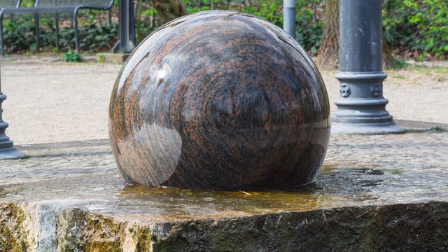 In einem öffentlichen Park dreht sich eine große Kugel aus Granit auf einer passenden Basis, geschmiert von einer dünnen Wasserschicht