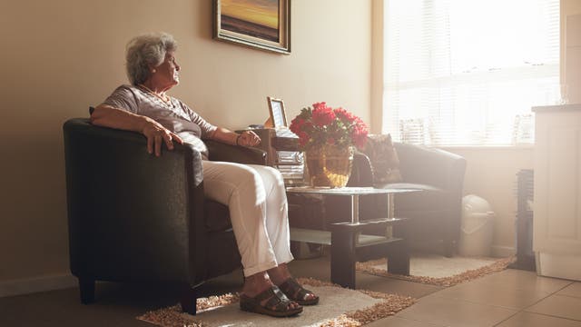 Eine Seniorin sitzt in einem Sessel, im Hintergrund ein hell erleuchtetes Fenster