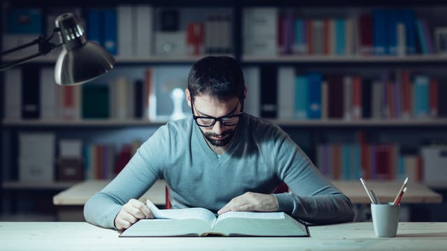 Ein junger Mann liest konzentriert in einem dicken Fachbuch 