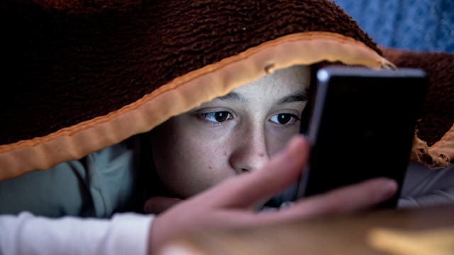 Kind mit Smartphone im Bett