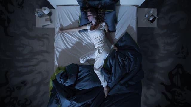 Eine Frau liegt nachts in ihrem Bett und schläft schlecht, weil sie einen Albtraum hat.