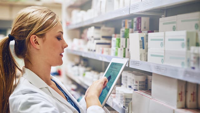 Eine Ärztin steht mit einem Tablet vor einem Medikamentenregal.