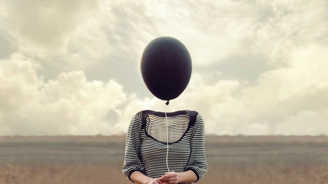 Ein Frau ohne Kopf hält einen schwarzen Luftballon in der Hand.