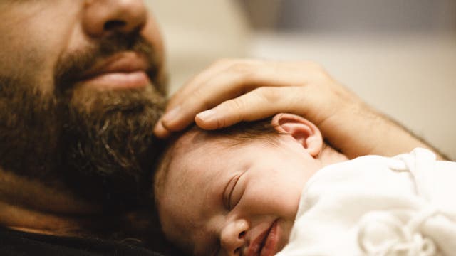 Ein Mann hält ein Baby nah an seinem Körper.