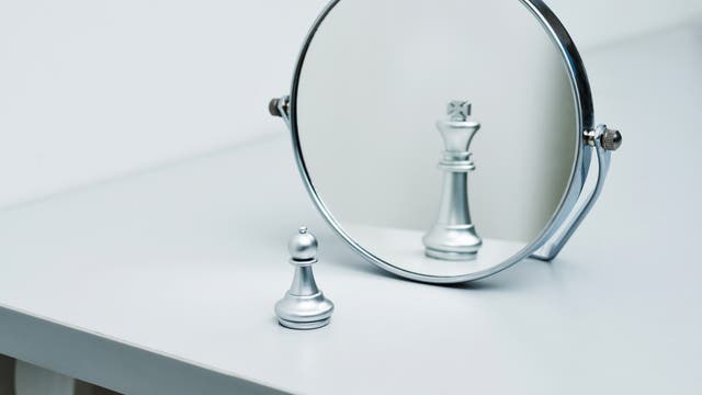 Eine Bauer-Schachfigur sieht sich in einem Spiegel als König. 