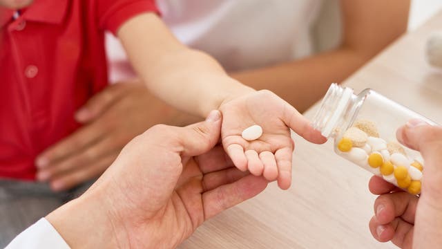 Ein Arzt gibt einem Kind eine Tablette in die Hand.