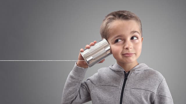 Ein kleiner Junge hält sich ein Dosentelefon ans Ohr.