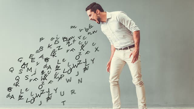 Ein Mann in einem weißen Hemd und beigen Hosen steht in einem Raum mit einem hellgrauen Hintergrund. Er beugt sich nach vorne und scheint zu schreien, während Buchstaben aus seinem Mund strömen und sich in der Luft verteilen. Die Buchstaben sind in verschiedenen Größen und scheinen zufällig angeordnet zu sein.