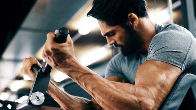 Äußerst muskulöser Mann trainiert seine Arme am Gerät