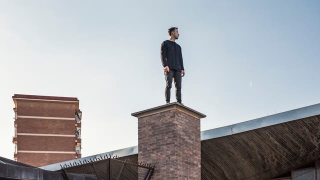 Ein Mann steht auf einem Schornstein und blickt über die Dächer 