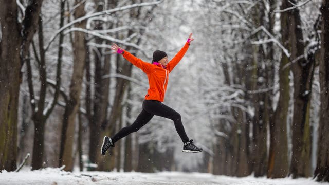 Joggerin macht Luftsprung in Winterlandschaft