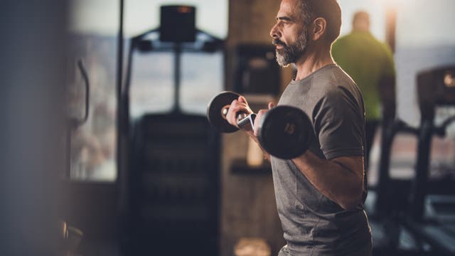 Ein älterer Mann trainiert mit einer Hantel seine Armmuskulatur im Fitness-Studio.
