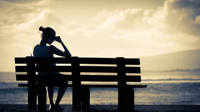 Frau sitzt im Schatten auf einer Bank