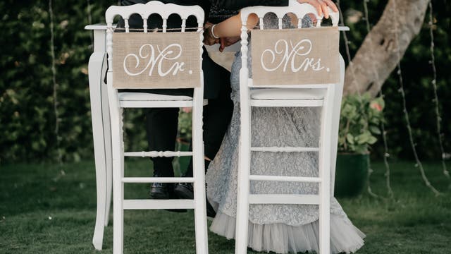 Brautpaar von hinten auf Stühlen, die mit Mr. & Mrs. beschriftet sind