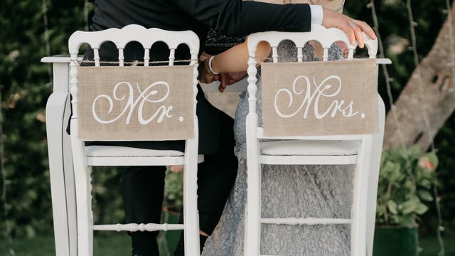Brautpaar von hinten auf Stühlen, die mit Mr. & Mrs. beschriftet sind