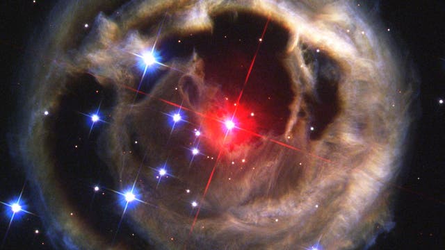 Im Zentrum der rot leuchtende Stern V838 Monocerotis, ringsherum ein konzentrischer Ring aus Lichtechos an Staubwolken.