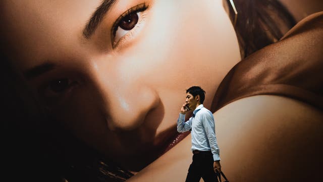 Asiate vor Werbeplakat mit Frauengesicht