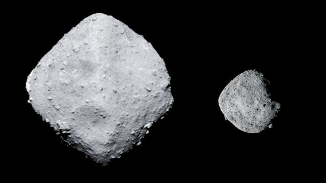 Das Bild zeigt zwei Asteroiden vor einem schwarzen Hintergrund. Links ist der größere Asteroid Ryugu, rechts der kleinere Asteroid Bennu. Beide Objekte haben eine unregelmäßige, felsige Oberfläche.