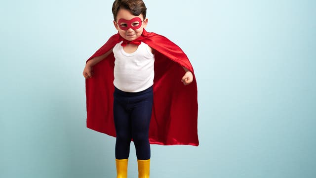 Ein Kind trägt eine Maske und ein rotes Cape. Es sieht aus wie ein Superheld.
