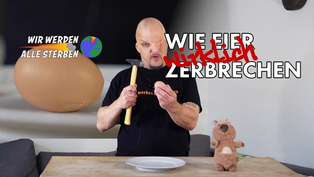 Eine Person steht vor einem Tisch und hält einen Hammer und ein Ei. Auf dem Tisch liegt ein leerer Teller. Links im Bild ist ein großes Ei mit der Aufschrift "WIR WERDEN ALLE STERBEN" und einer Weltkugel daneben. Rechts im Bild steht in großen Buchstaben "WIE EIER wirklich ZERBRECHEN". Ein Plüschtier steht ebenfalls auf dem Tisch. Die Szene vermittelt eine humorvolle Darstellung des Eierzerbrechens.