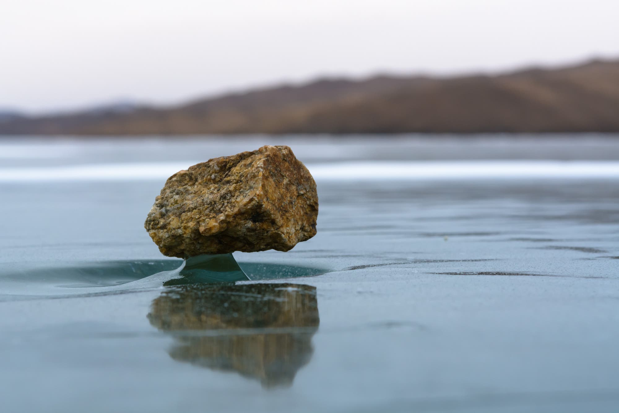 Wie eine Skulptur auf einem Podest erhebt sich über dem Baikalsee ein Stein aus einer Mulde im Eis