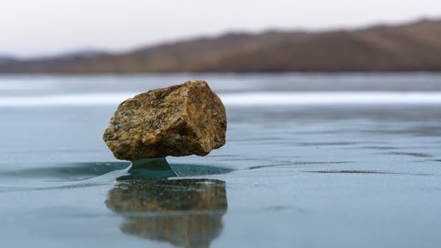 Wie eine Skulptur auf einem Podest erhebt sich über dem Baikalsee ein Stein aus einer Mulde im Eis