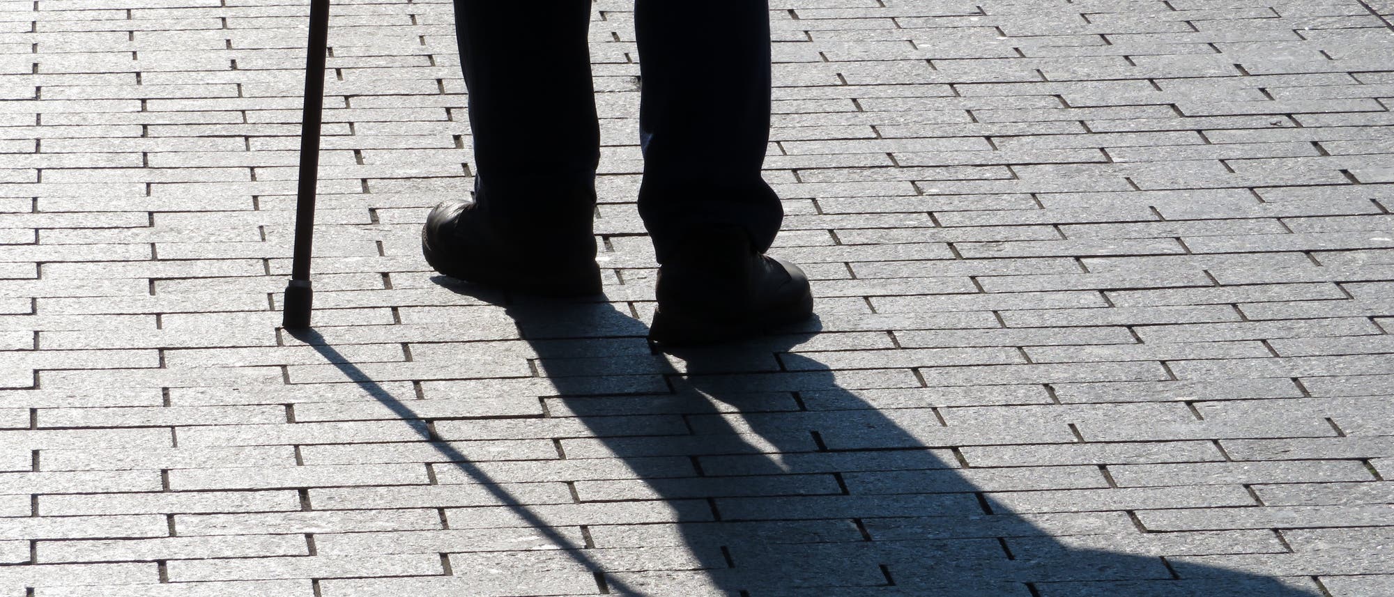 Silhouette und Schatten der Beine eines alten Mannes, der am Stock geht Silhouette und Schatten der Beine eines alten Mannes, der am Stock geht
