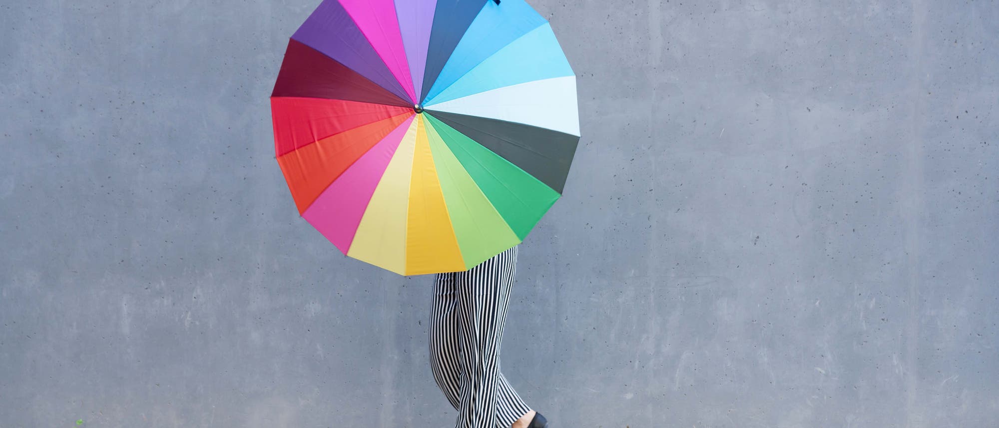Mensch verdeckt hinter einem Schirm in Regenbogenfarben Mensch verdeckt hinter einem Schirm in Regenbogenfarben