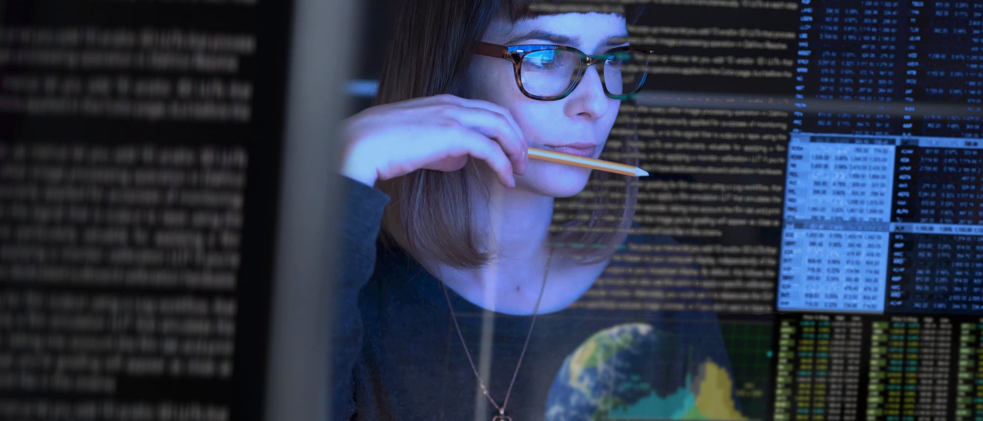 Junge Frau mit Brille studiert Datenreihen auf einem Bildschirm