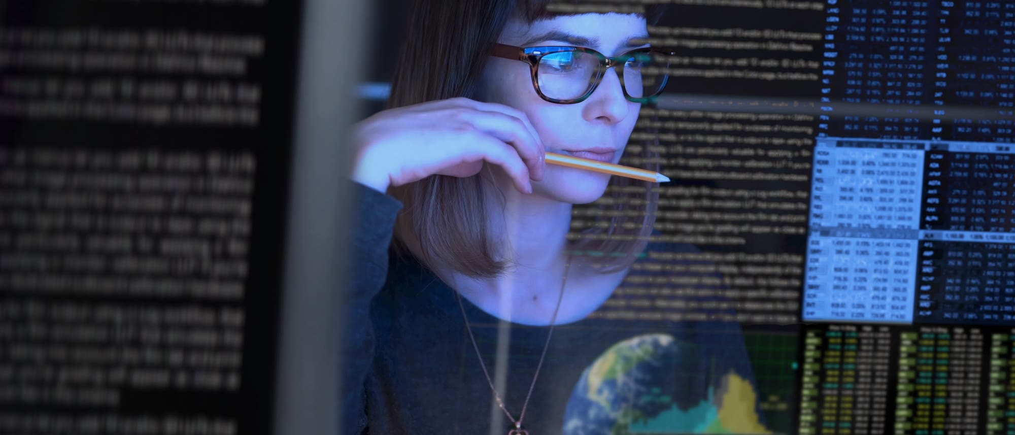 Junge Frau mit Brille studiert Datenreihen auf einem Bildschirm Junge Frau mit Brille studiert Datenreihen auf einem Bildschirm