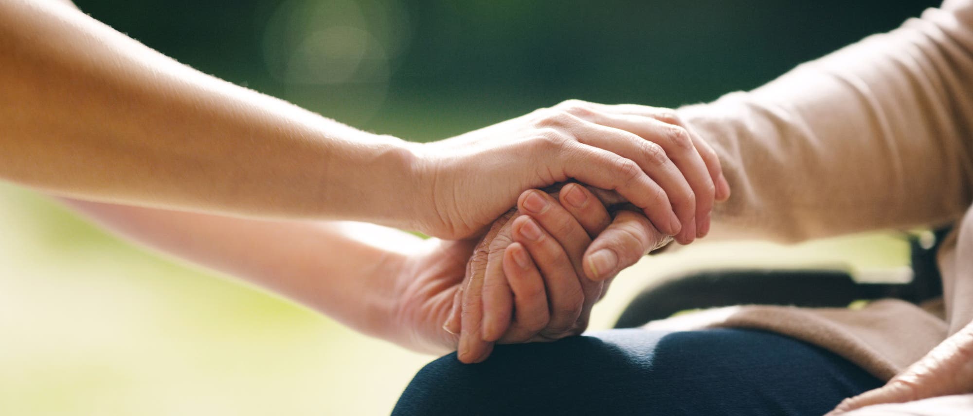 Zwei Hände ergreifen die Hand eines Menschen im Rollstuhl Zwei Hände ergreifen die Hand eines Menschen im Rollstuhl