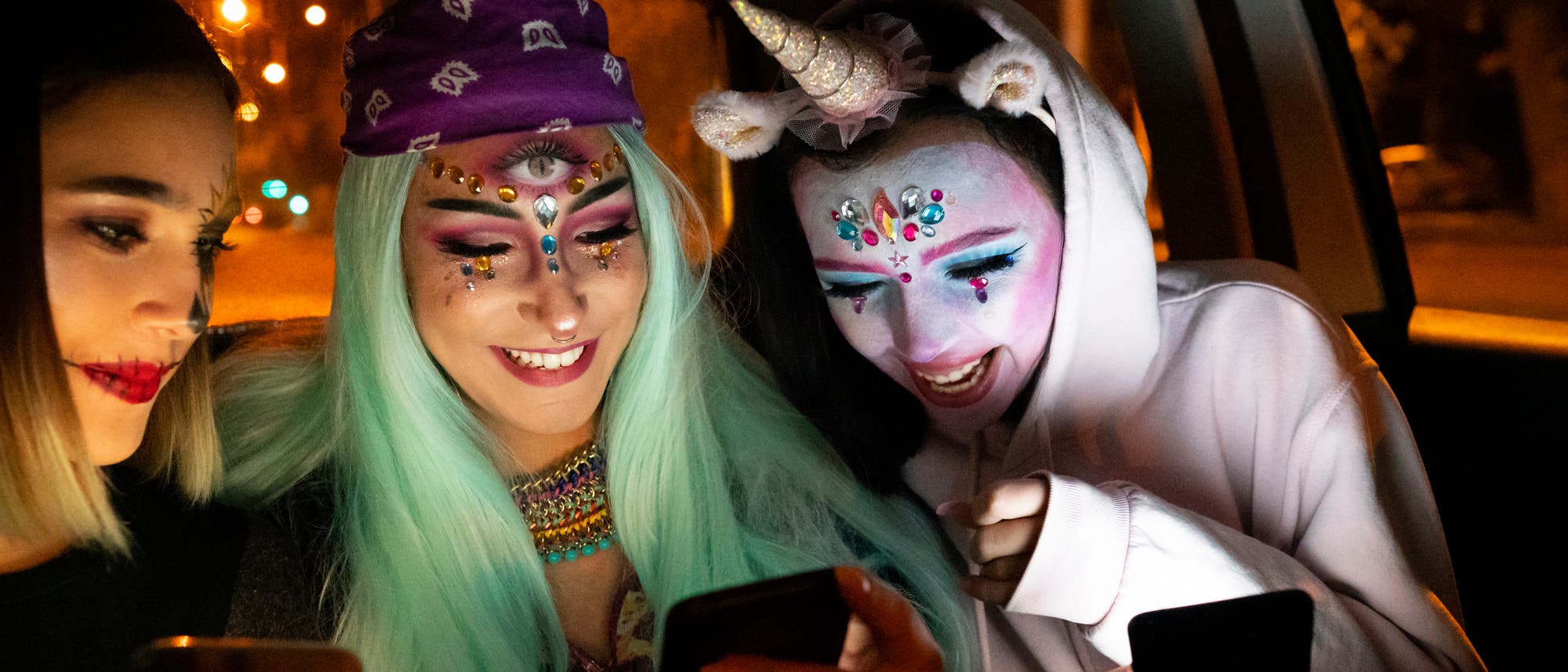 Zwei junge Frauen und ein Einhorn kommunizieren auf dem Weg zum Kostümball mit sich und ihren Smartphones Zwei junge Frauen und ein Einhorn kommunizieren auf dem Weg zum Kostümball mit sich und ihren Smartphones