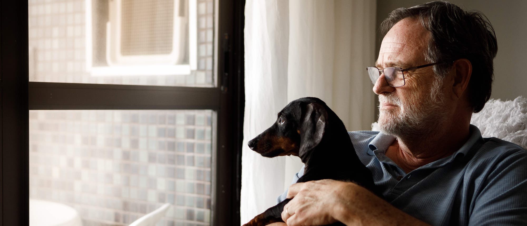 Mann mit Hund guckt nachdenklich aus dem Fenster Mann mit Hund guckt nachdenklich aus dem Fenster
