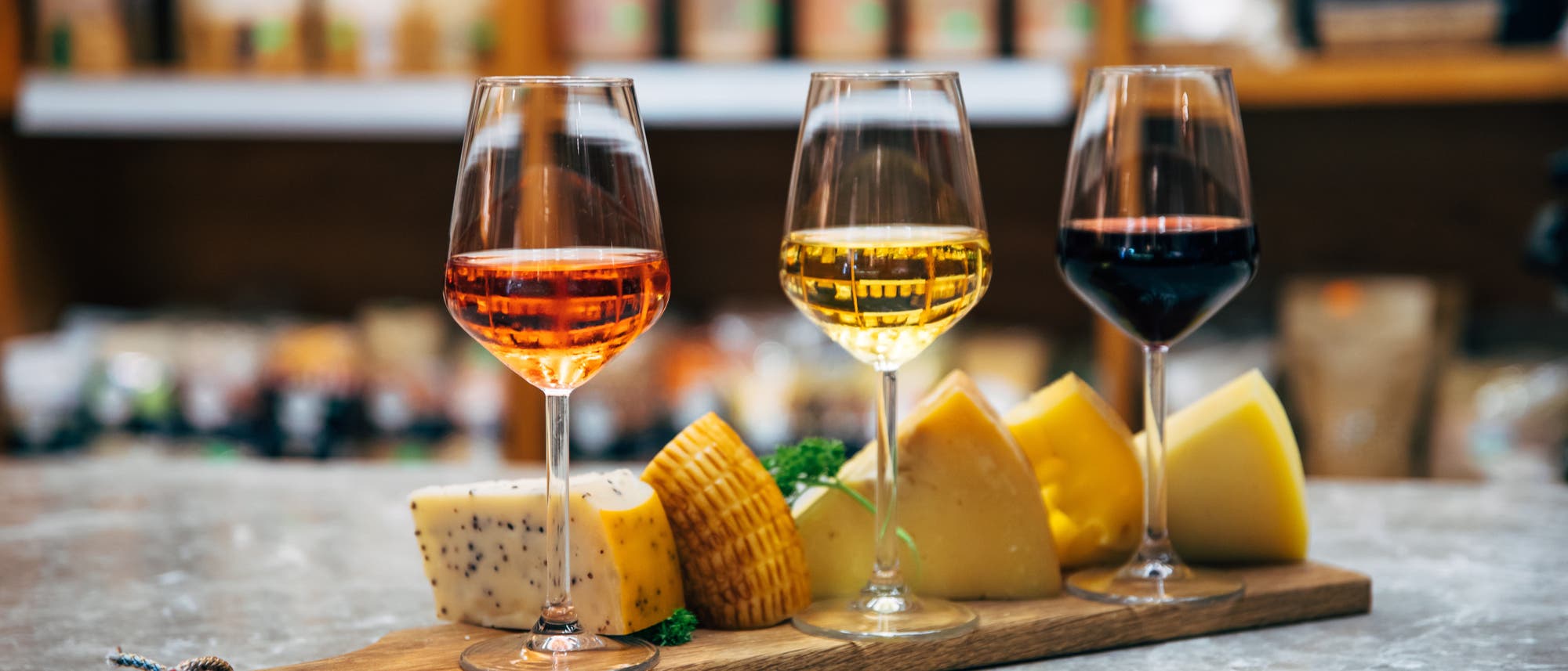 Drei Gläser Wein und mehrere Käsesorten auf einem Holzbrett