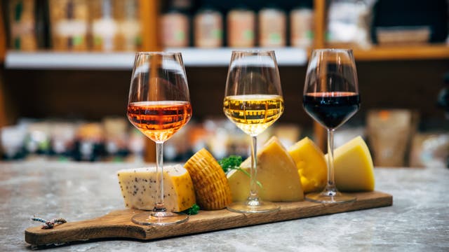 Drei Gläser Wein und mehrere Käsesorten auf einem Holzbrett