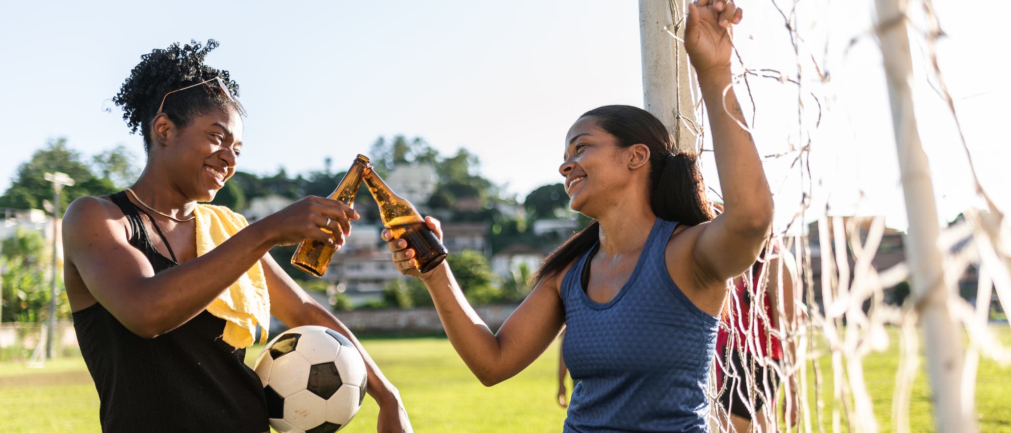 Zwei junge Fußballerinnen stoßen auf dem Feld mit einem Bier an. Zwei junge Fußballerinnen stoßen auf dem Feld mit einem Bier an.