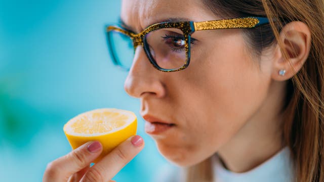 Frau mit Brille hält sich eine halbe Zitrone unter die Nase und riecht konzentriert daran.