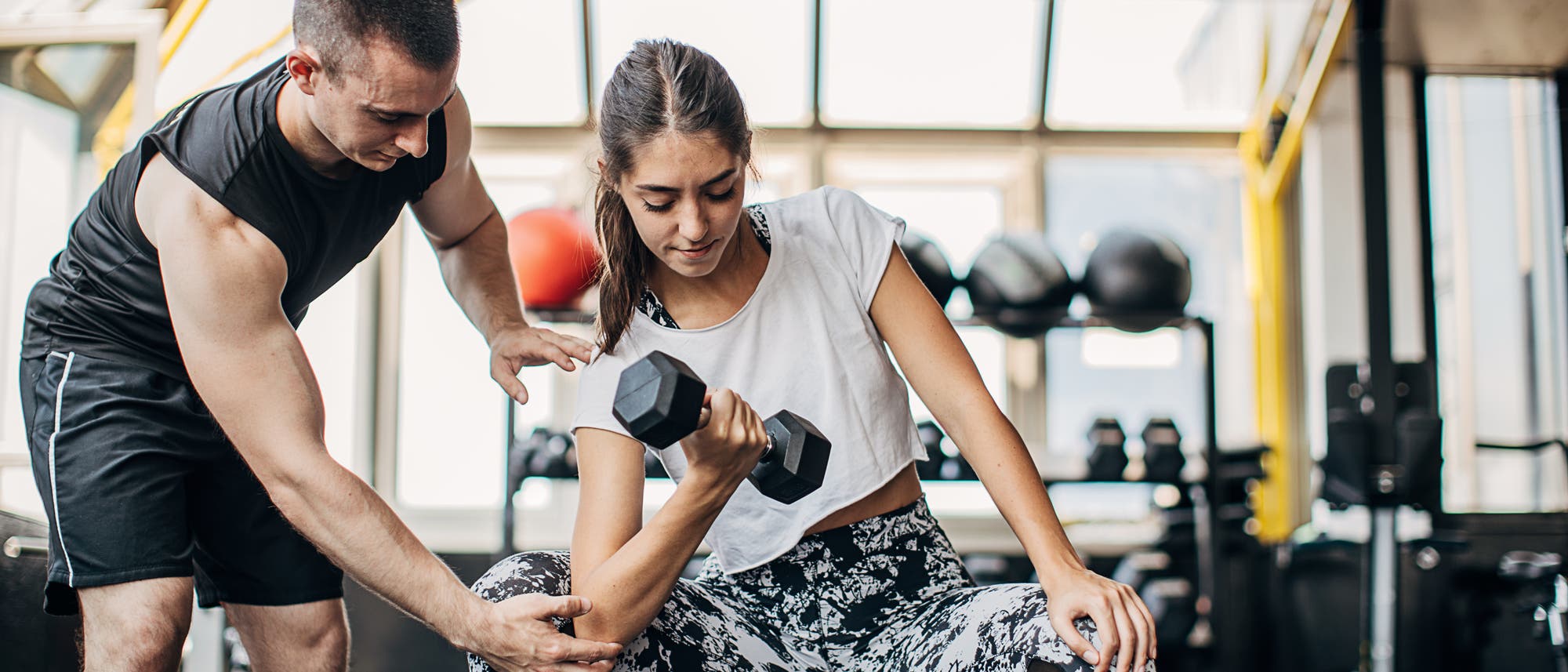 Frau beim Krafttraining mit Hantel, begleitet von einem Fitnesstrainer Frau beim Krafttraining mit Hantel, begleitet von einem Fitnesstrainer