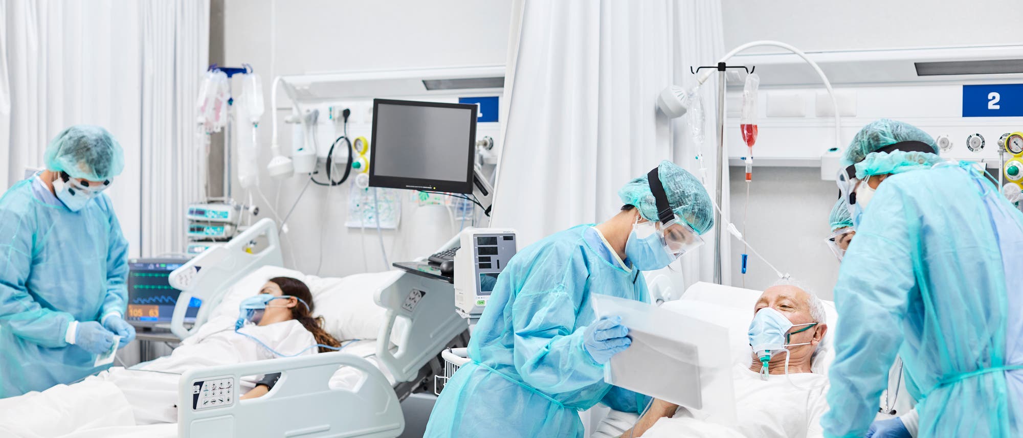 Ein älterer Patient und eine jüngere Patientin mit MNS in Intensivbetten, umgeben von Ärztinnen und Ärzten in Schutzausrüstung. Ein älterer Patient und eine jüngere Patientin mit MNS in Intensivbetten, umgeben von Ärztinnen und Ärzten in Schutzausrüstung.