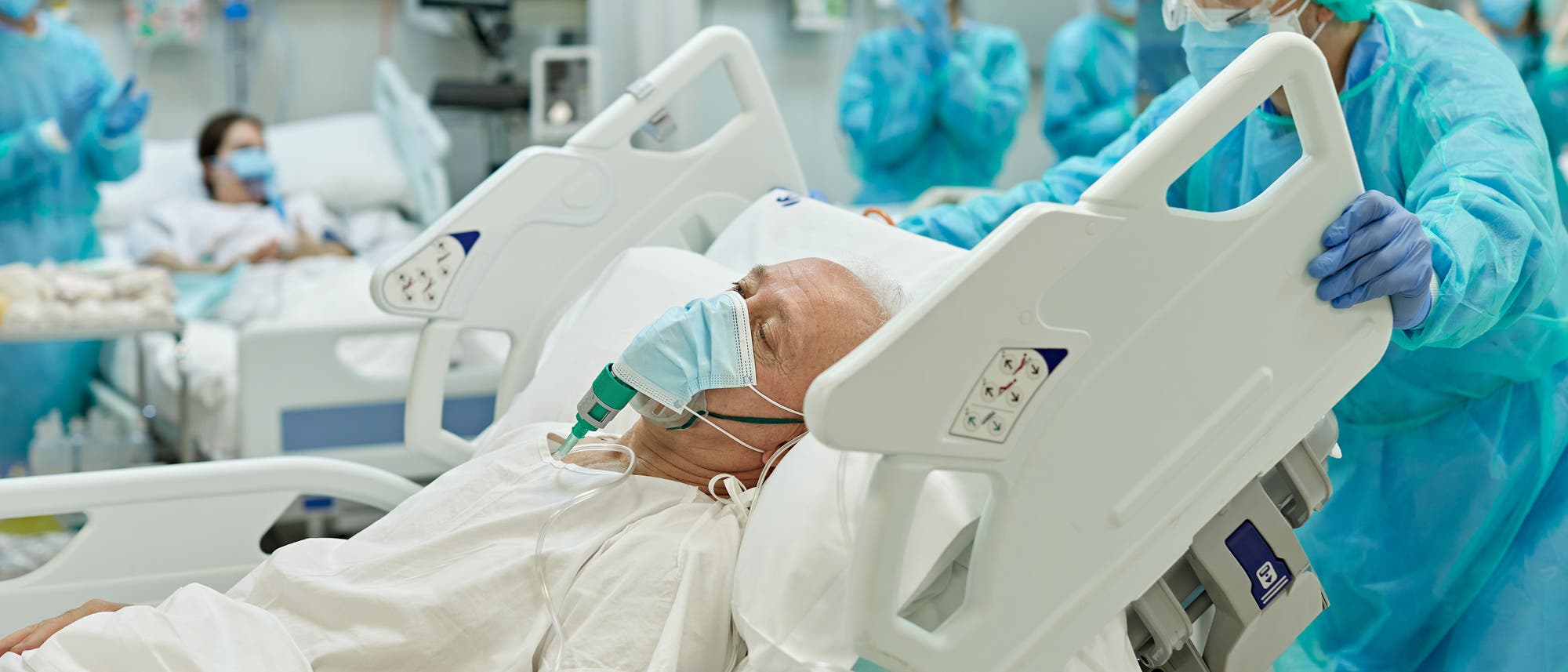 Beatmeter älterer Mann im Krankenbett wird von medizinischem Personal geschoben- Beatmeter älterer Mann im Krankenbett wird von medizinischem Personal geschoben-