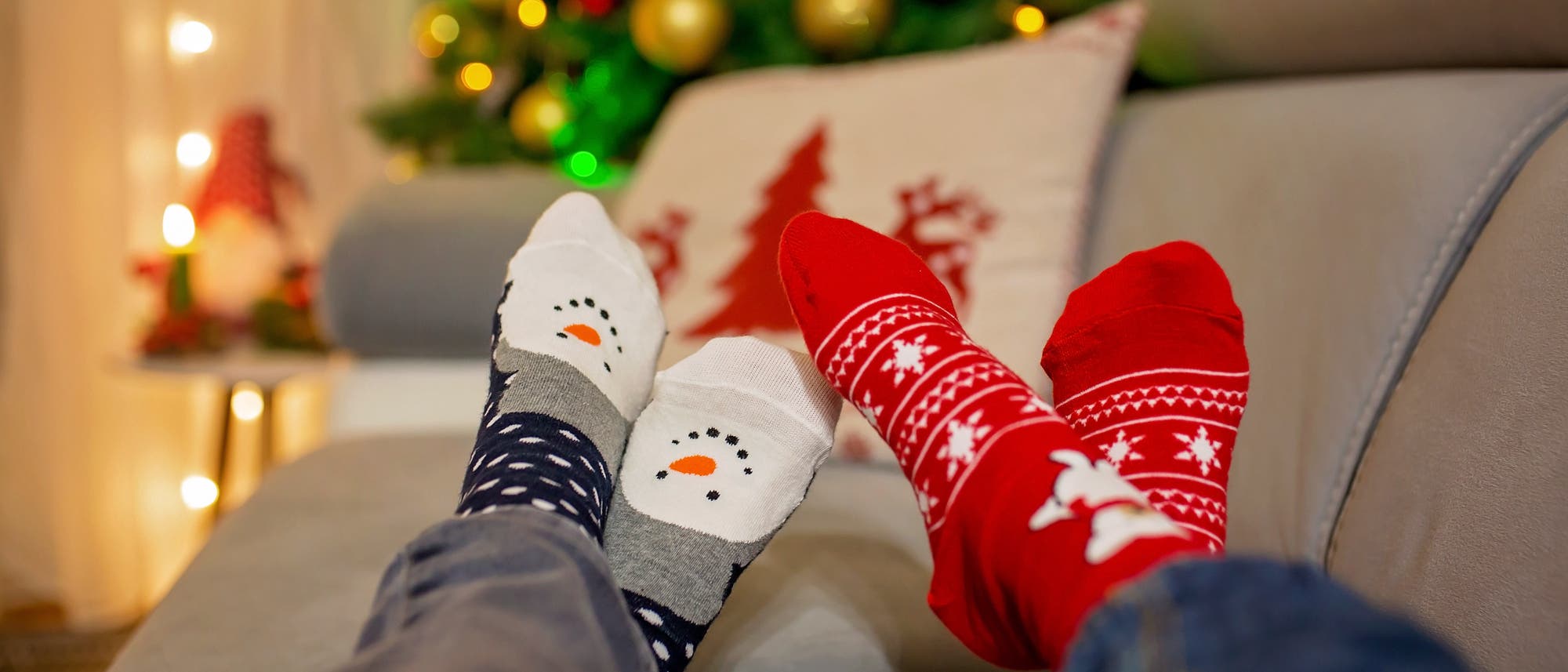 Füße in Weihnachtsstrümpfen auf dem Sofa vorm Weihnachtsbaum