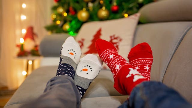 Füße in Weihnachtsstrümpfen auf dem Sofa vorm Weihnachtsbaum