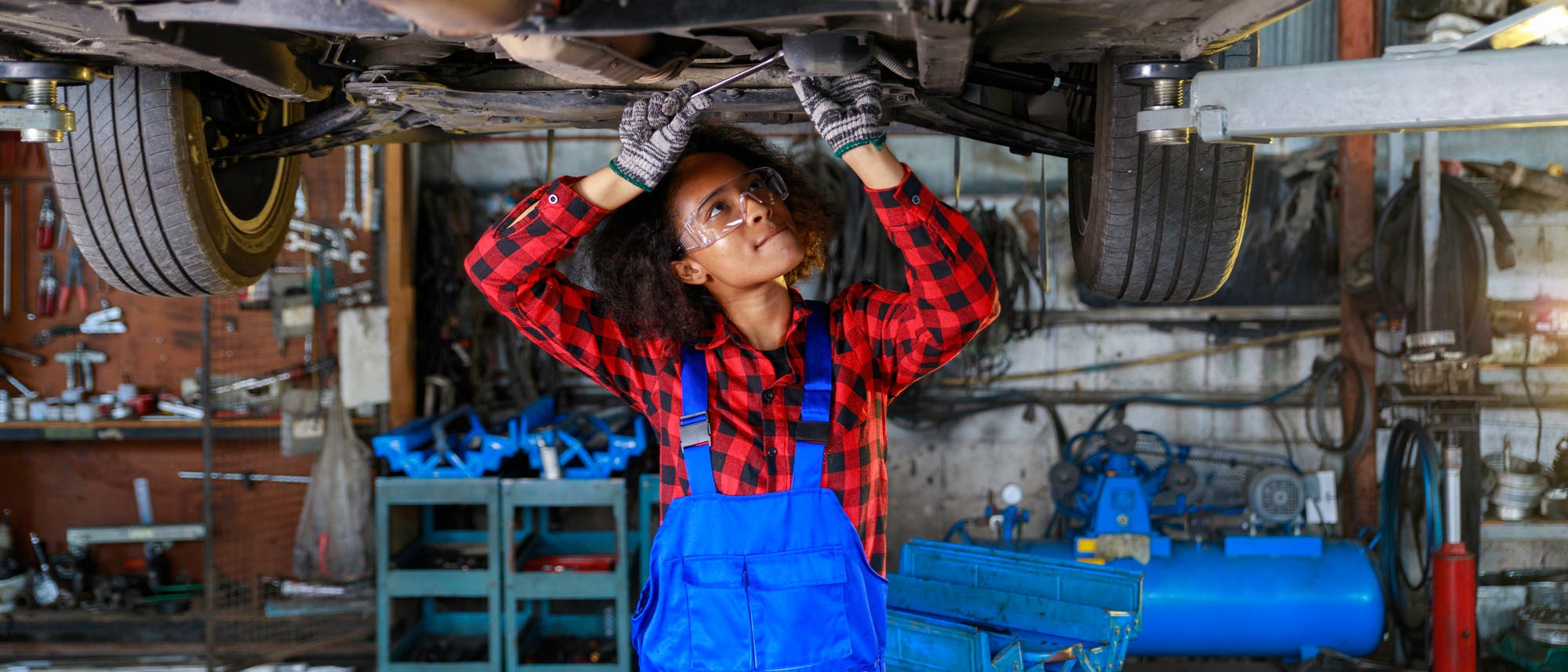 Automechanikerin steht unter einem Auto und repariert es Automechanikerin steht unter einem Auto und repariert es