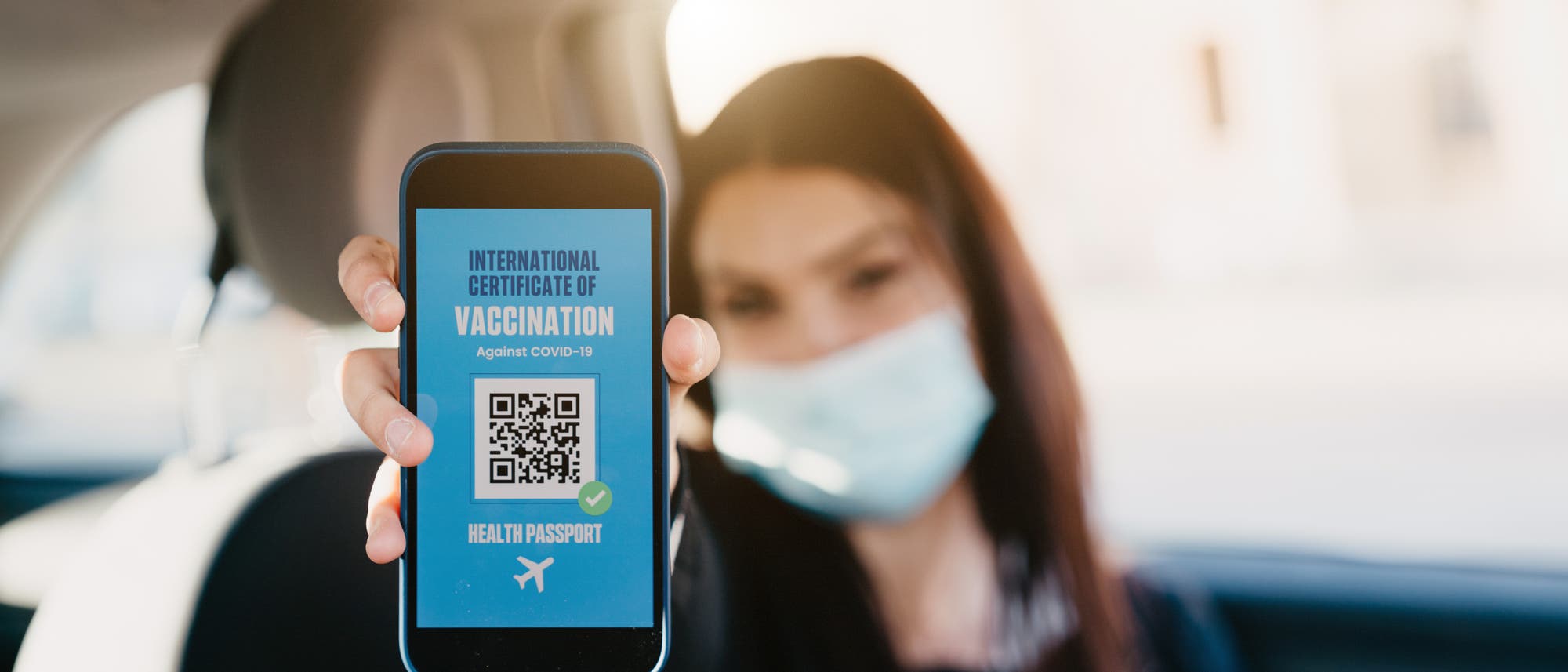 Frau im Auto zeigt App mit internationalem Impfnachweis und QR-Code vor. Frau im Auto zeigt App mit internationalem Impfnachweis und QR-Code vor.