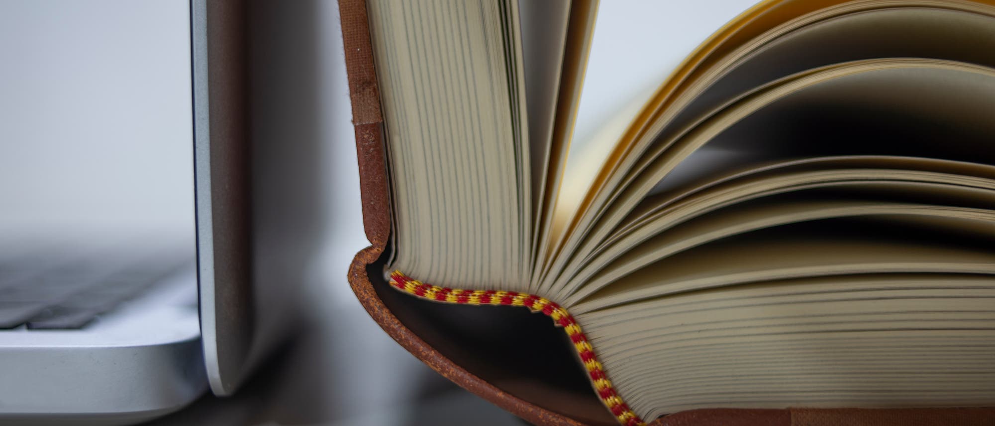 Ein altes Hardcover-Buch lehnt aufgeklappt an einem Laptop. Ein altes Hardcover-Buch lehnt aufgeklappt an einem Laptop.